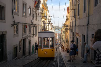 A yellow tram climbing a steep street in Lisbon